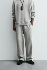 Pantalón de jogging gris con corte relaxed fit, cintura elástica ajustable con cordón interior, bolsillos laterales y traseros de vivo, y banda lateral color crema.
