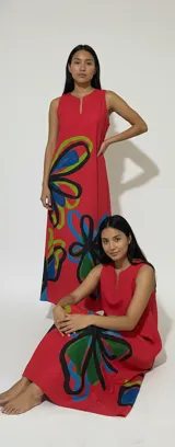 Vestido largo rojo de lino liviano, con silueta amplia y fluida, escote con pequeña abertura frontal, bolsillos laterales y estampado de flores abstractas en tonos verde, azul y negro. Diseño exclusivo de la marca con tintas ecológicas. Hecho en Uruguay.