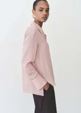 Camisa celeste con rayas verticales finas, de tejido fluido, manga larga abotonada, cuello camisero y corte recto.