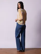 Blusa de gasa estampada a rayas verticales en tonos celeste, lila, naranja y marrón. Tiene cuello a la base con escote en V y botones. Delantera con bolsillo aplicado. Largo de manga regulable con presilla y botón. Terminación anudada opcional.