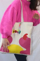 Bolso tipo tote de lona color crudo con asas de tela. Estampado con el logo 'picú' y diseño abstracto en colores amarillo, verde y fucsia.