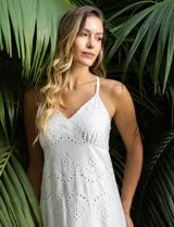 Vestido blanco de broderie con escote en V, corte bajo el busto y breteles finos cruzados en la espalda. Tiene forro interno a tono y largo midi.