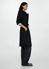 Trench coat negro con cuello de solapa, doble botonadura, trabillas en los puños, cinturón ajustable y abertura posterior en el bajo.