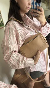 Cartera bandolera de cuero color camel, con correa de cuero trenzada en tonos beige y negro. Forro interior de tela estampada.