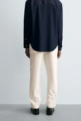 Pantalón chino negro de corte relajado (relaxed fit) con tiro medio, confeccionado en algodón con elasticidad. Presenta bolsillos delanteros y bolsillos traseros de vivo, con cierre frontal de cremallera y botón.