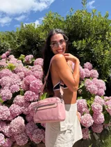 Bandolera color rosa viejo con detalles en cuero marrón claro, múltiples cremalleras metálicas y herrajes plateados. Incluye correa ancha ajustable con el logo de la marca.