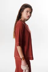 Blusa de lino color beige claro, con mangas 3/4 y cuello redondo. Presenta pespuntes a contratono en el centro, puños y ruedo.