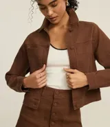 Campera marrón de sarga con textura cotelê, corte regular, cuello inglés, manga larga, abotonada y con bolsillos delanteros.