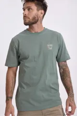 Remera de algodón color verde salvia, con cuello redondo y manga corta. Presenta un pequeño parche estampado en el pecho con un diseño gráfico.