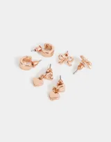 Set de tres pares de aros bañados en oro rosa: un par de aros tipo botón con forma de moño, un par colgantes con dije de corazón y un par de aros tipo argolla.