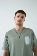 Remera verde militar de corte oversized, con cuello redondo y mangas cortas. Presenta un estampado con texto y figuras geométricas en el frente.