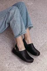 Zuecos negros de cuero con textura de pelo, diseño cerrado con hebilla lateral y tira ajustable en el talón.