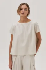 Blusa color crema de lino metalizado, de calce recto, con cuello bote y mangas cortas.