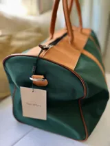 Bolso tipo duffel de lona con estampado de camuflaje y detalles en cuero marrón. Tiene doble asa de mano y correa de hombro ajustable y extraíble.