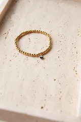 Pulsera elástica dorada con bolitas de acero quirúrgico hipoalergénico y dije colgante de ojo turco.