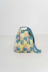 Bolso tipo bucket tejido con diseño geométrico en tonos combinados: amarillo, celeste y beige. Posee cordón ajustable y correa ancha al tono para llevar al hombro o cruzado.