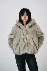 Chaqueta corta de pelo sintético color gris con capucha y cierre frontal con broches metálicos.