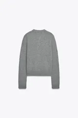 Chaqueta de punto color rosa pálido, con cuello redondo y cierre frontal de botones oscuros. Presenta mangas largas y un corte a la cintura.