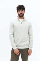 Buzo de algodón color verde musgo, con cuello alto y cierre frontal parcial. Presenta puños y cintura acanalados, y un pequeño logo bordado en el pecho.