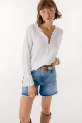 Blusa blanca de lino con botones de nácar, volados en el escote y mangas largas con puños acampanados. Corte recto y holgado.