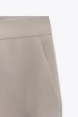 Pantalón de vestir color beige, de tiro alto, corte recto y bolsillos laterales.