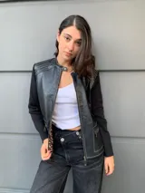 Campera negra con cuerpo de cuero sintético y mangas largas de tejido de punto fino. Presenta cierre frontal con cremallera, cuello redondo y bolsillos con cierre en el frente. Detalles de costuras en color blanco.