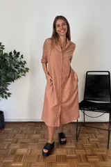 Vestido camisero largo color terracota/bronce, de manga larga con puños remangados, cuello solapa y cierre frontal de botones. Tiene un corte amplio y bolsillos laterales.