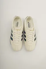 Championes Adidas Tokyo color crema con detalles en negro, con las tres tiras características de la marca en los laterales.