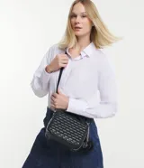 Bolso transversal tipo camera bag, color negro, hecho en material sintético texturizado. Tiene correa fina ajustable y removible, cierre por cremallera y colgante pompón.