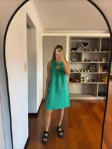 Vestido corto verde esmeralda, sin mangas, con cuello redondo y abertura con lazos en el pecho.