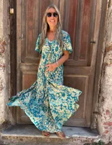 Vestido largo de seda, fluido y amplio, con mangas cortas y bolsillos laterales. Presenta un estampado en tonos turquesa y beige/crema.