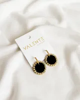 Aros colgantes con forma circular, hechos de acrílico negro con borde dorado con strass. El aro es de acero dorado.