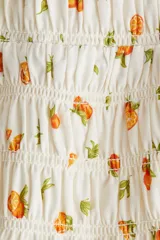 Vestido corto blanco con estampado de naranjas, breteles anchos y escote en U. Presenta frunces en el busto y falda con volados.