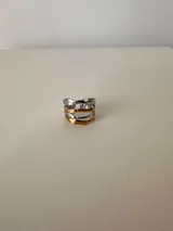 Anillo plateado con detalles dorados, ajustable entre 16 mm y 19 mm, fabricado en acero quirúrgico hipoalergénico.
