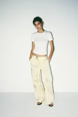 Pantalón cargo color blanco hueso, de tiro medio, corte ancho y tela satinada. Incluye cinturón con hebilla metálica, bolsillos delanteros, laterales con cierre y traseros de vivo. Cierre frontal con cremallera y ganchos metálicos.