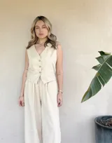 Chaleco color crema con cuello en V y cierre con botones. Diseño con bolsillos frontales y corte recto.