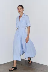 Vestido camisero midi de popelín a rayas verticales celestes y blancas, con cuello solapa, manga corta, bolsillos de plastrón con solapa en el pecho, cinturón de lazo ajustable y cierre frontal con botones.