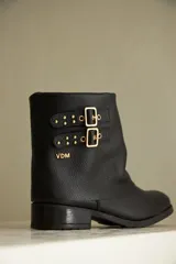 Bota de caña corta negra confeccionada en cuero, con detalle de botamanga y hebillas doradas.