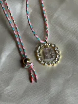 Collar con dije circular dorado con strass y letra 'A' en el centro, con cordón trenzado multicolor y cierre ajustable.