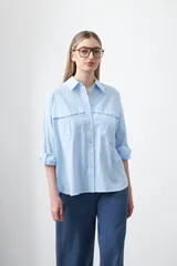 Camisa de algodón color celeste claro, con diseño utilitario, bolsillos frontales de estilo cargo con tapa y costuras a contratono. Presenta un calce relajado y largo levemente posterior.