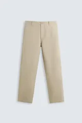 Pantalón chino color beige, de corte recto, con bolsillos laterales y traseros. Se ajusta a la cintura con cinturón de cuero marrón.