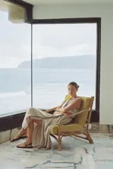 Vestido midi de lino color beige, con escote cruzado en pico y sin mangas. Presenta vivos a contraste en negro y cinturón con hebilla forrada. Cierre frontal con botones.