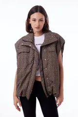 Chaleco puffer impermeable con estampado geométrico en tonos marrones y negros, forrado con tafeta negra. Tiene dos bolsillos frontales, bolsillos laterales ocultos, cierre desmontable, broches snap y elástico ajustable con tanca en ruedo.