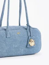 Cartera tipo baulito color celeste, confeccionada en denim, con manijas de tela. Incluye un charm colgante de mariquita dorada.