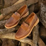 Mocasín de cuero vacuno color marrón, con detalle de antifaz en gamuza. Tiene taco de madera foliado en cuero de 2,5cm y entre suela de goma de 1cm.