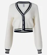 Cardigan corto de punto color crema con escote en V ribeteado en negro y blanco. Presenta cierre frontal de botones negros y puños con el mismo ribete a rayas. Las mangas son largas y ligeramente abullonadas.
