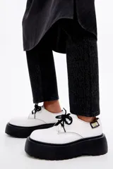 Zapato blucher acordonado de piel color blanco con ojetes metálicos y etiqueta textil personalizada en el lateral. Plataforma de goma logotipada color negro.