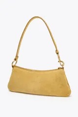 Bolso de hombro color mostaza, confeccionado en gamuza. Tiene asa corta, cierre superior con cremallera y herrajes dorados.