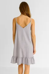 Vestido corto color beige claro, de lino, con escote en V y breteles finos ajustables. Presenta un ruedo con volado.