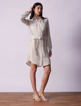 Vestido camisero corto a rayas verticales color beige, con cuello con solapa, abertura central con botones, bolsillos aplicados en el pecho y lazo de ajuste en la cintura.